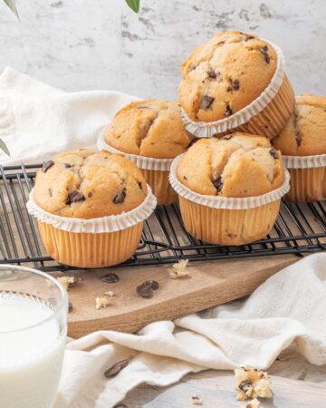 Chocolate chip muffins on a baking rack and glasses of milk on a white kitchen countertop